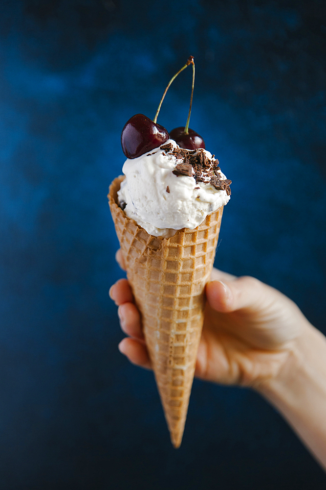 Hand holding ice cream cone with cherries