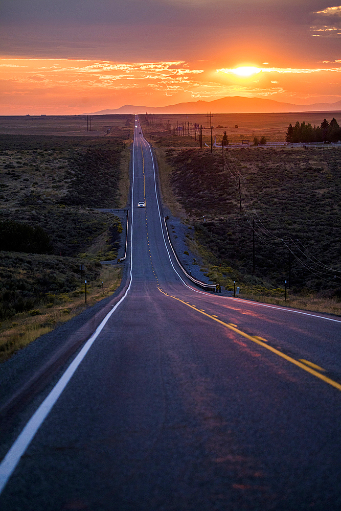 Cars driving on remote road at sunset