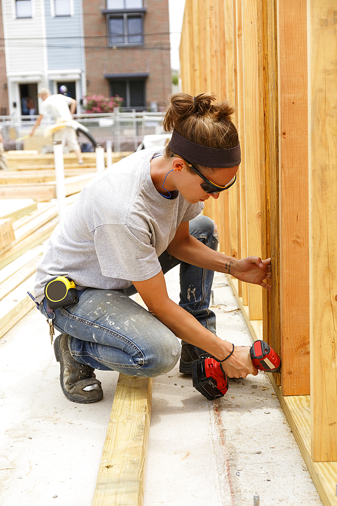 Caucasian woman drilling lumber at construction site