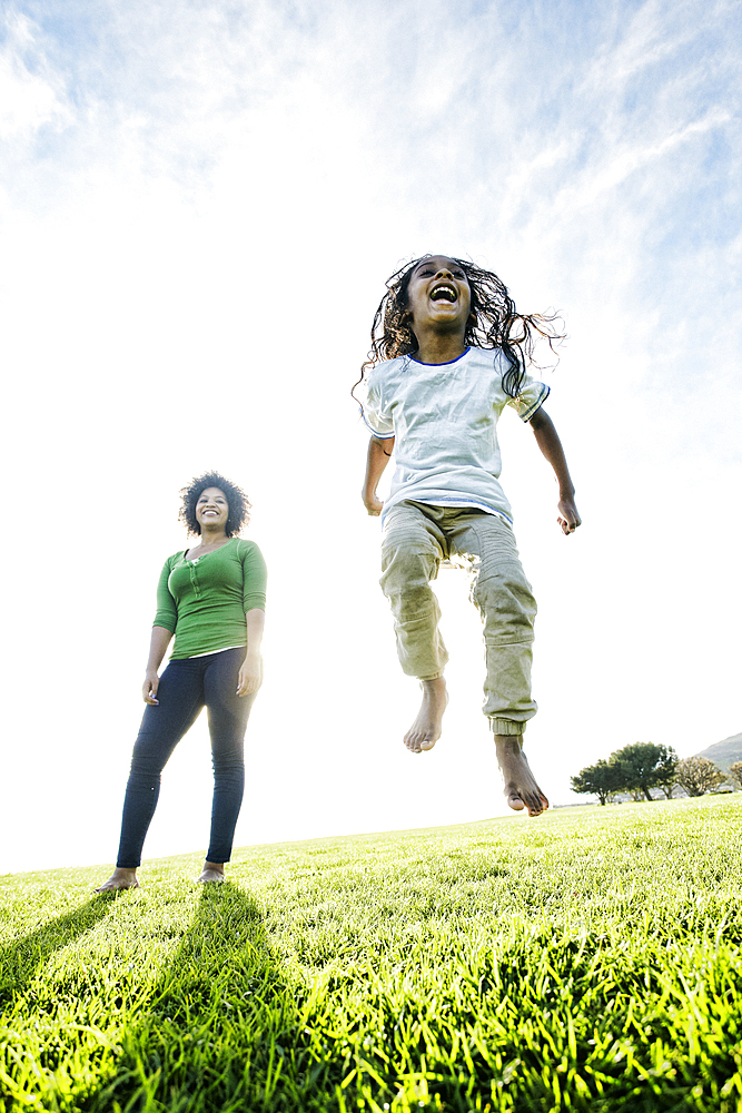 Mixed race mother watching daughter jumping in the grass