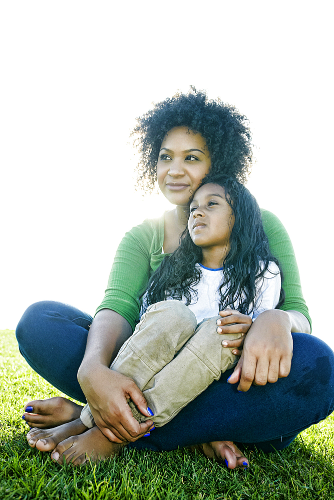 Portrait of pensive mixed race mother and daughter sitting in grass