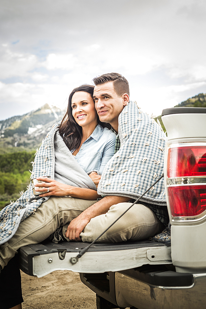 Couple wrapped in blanket sitting on bed of pick-up truck