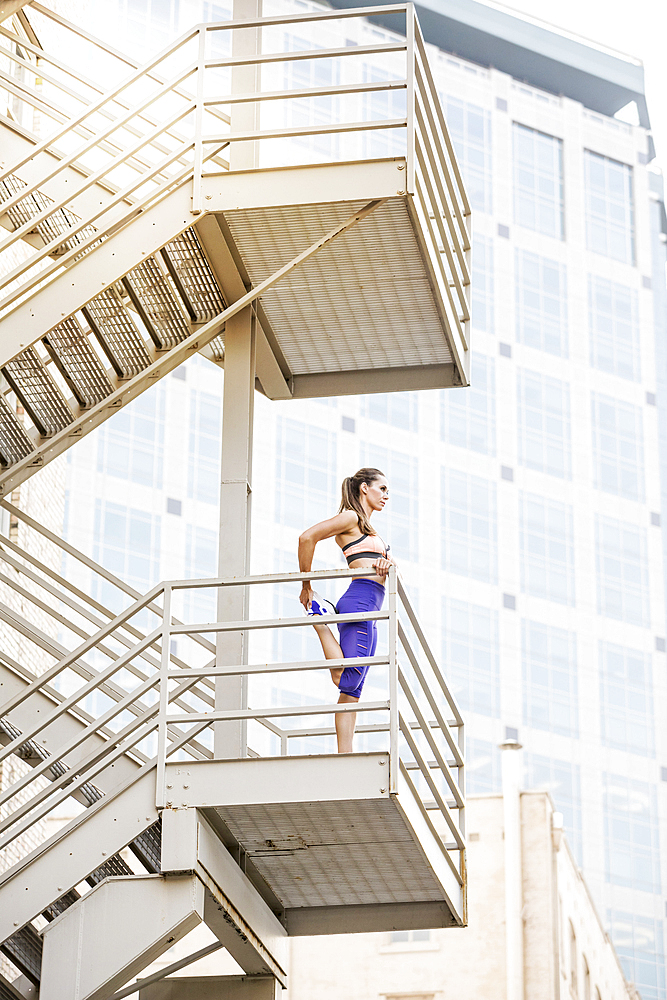 Caucasian woman stretching leg on urban staircase