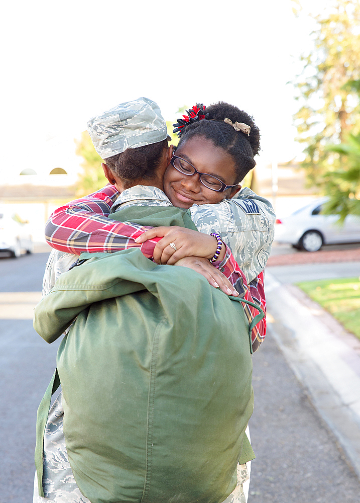 Black woman soldier hugging daughter in street