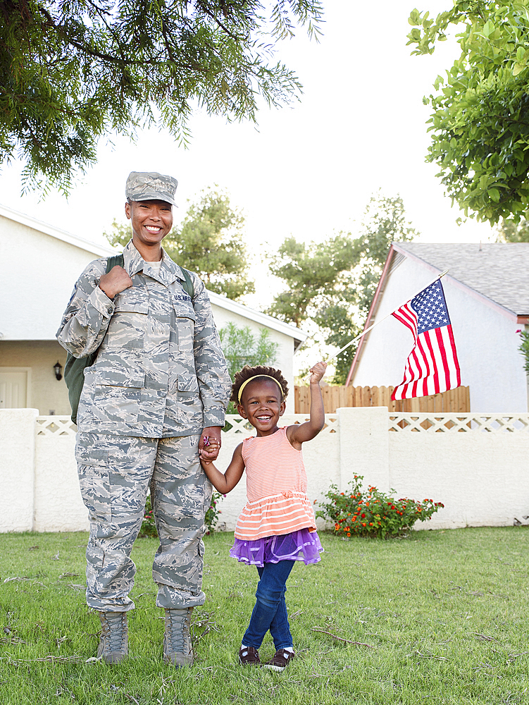 Smiling black woman soldier with daughter waving American flag