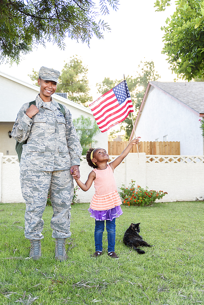 Smiling black woman soldier with daughter waving American flag