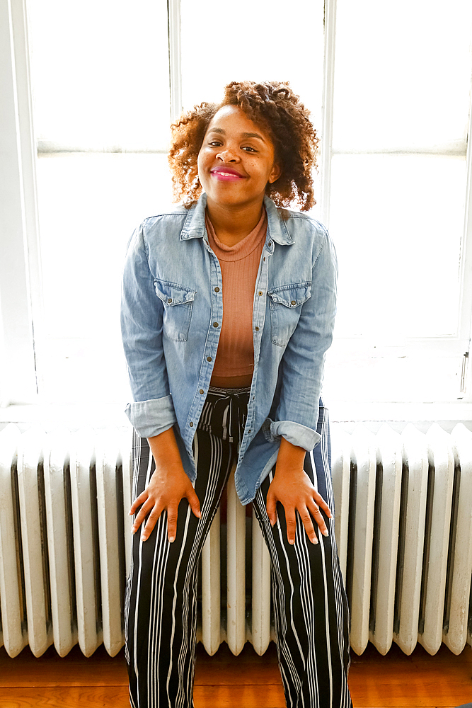 Smiling mixed race woman sitting on radiator