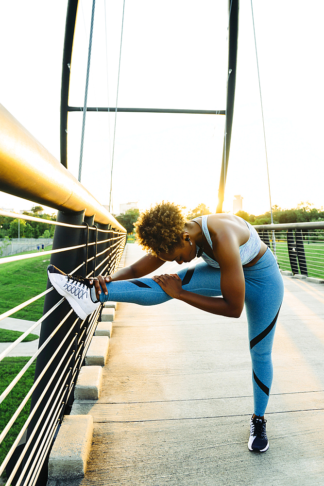 Mixed race woman stretching leg on bridge railing