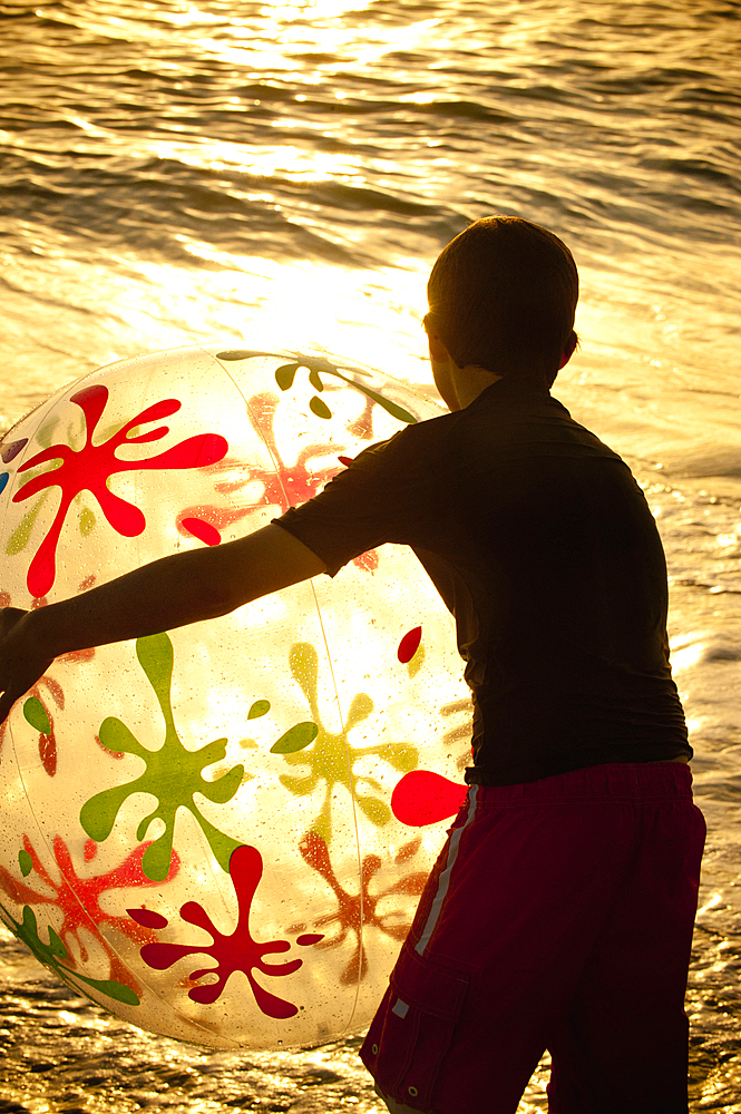 Silhouette of Caucasian boy holding beach ball at sunset