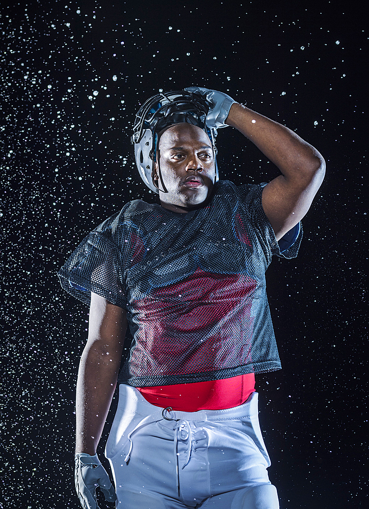 Water splashing on Black football player lifting helmet