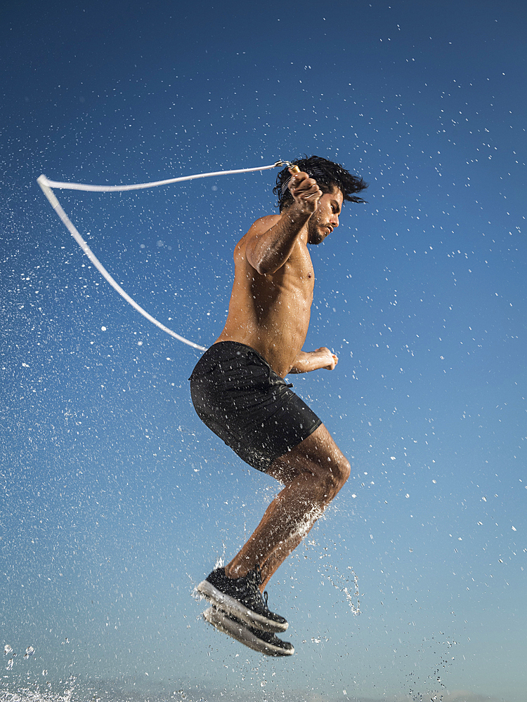 Water splashing on Hispanic man jumping rope