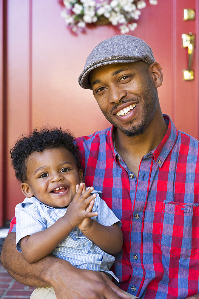 Smiling mixed race father and baby son sitting on front stoop