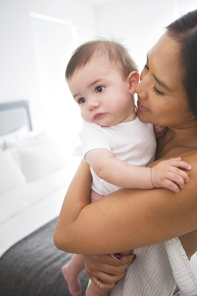 Mother hugging baby son in bedroom