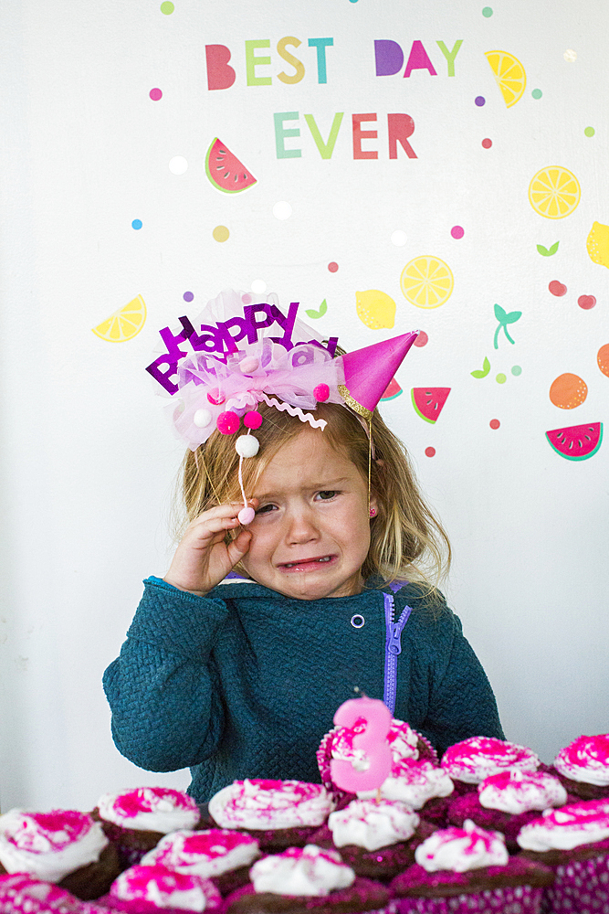 Caucasian girl crying over tray of cupcakes for birthday