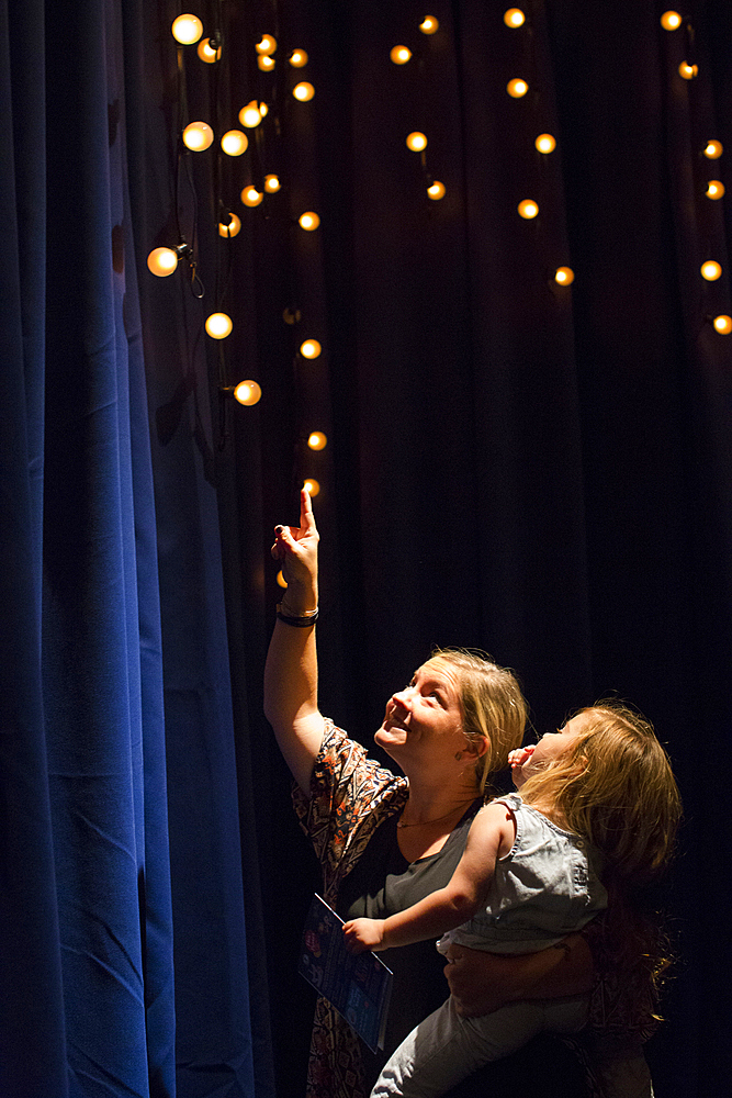 Caucasian mother and daughter looking up at blue curtain