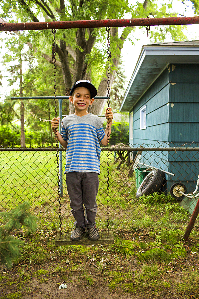 Smiling mixed race boy standing on backyard swing