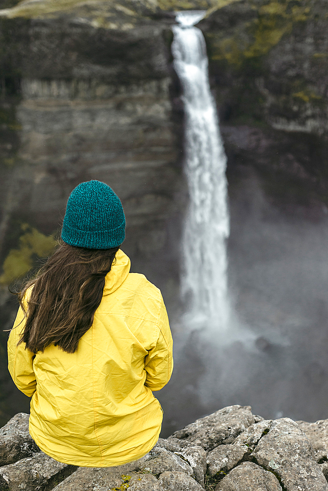 Caucasian woman sitting on cliff admiring waterfall