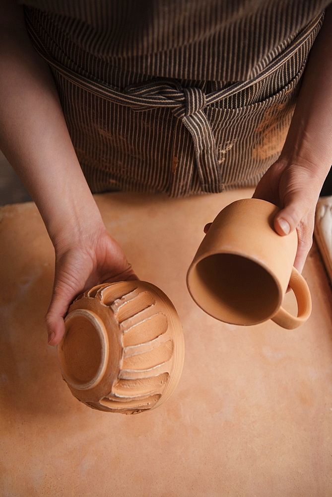 Hand of Caucasian woman holding pottery cup and bowl