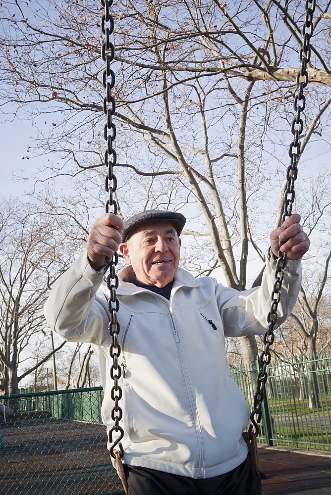 Carefree Hispanic man on swing in park