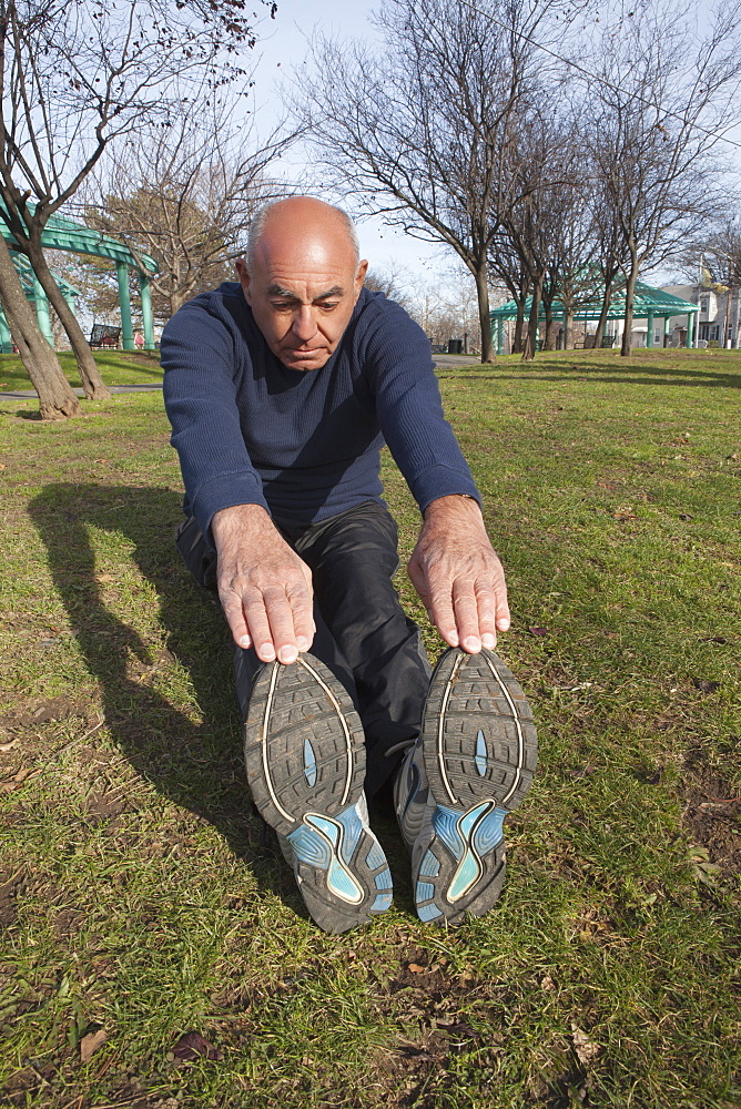 Hispanic man sitting on grass in park stretching legs