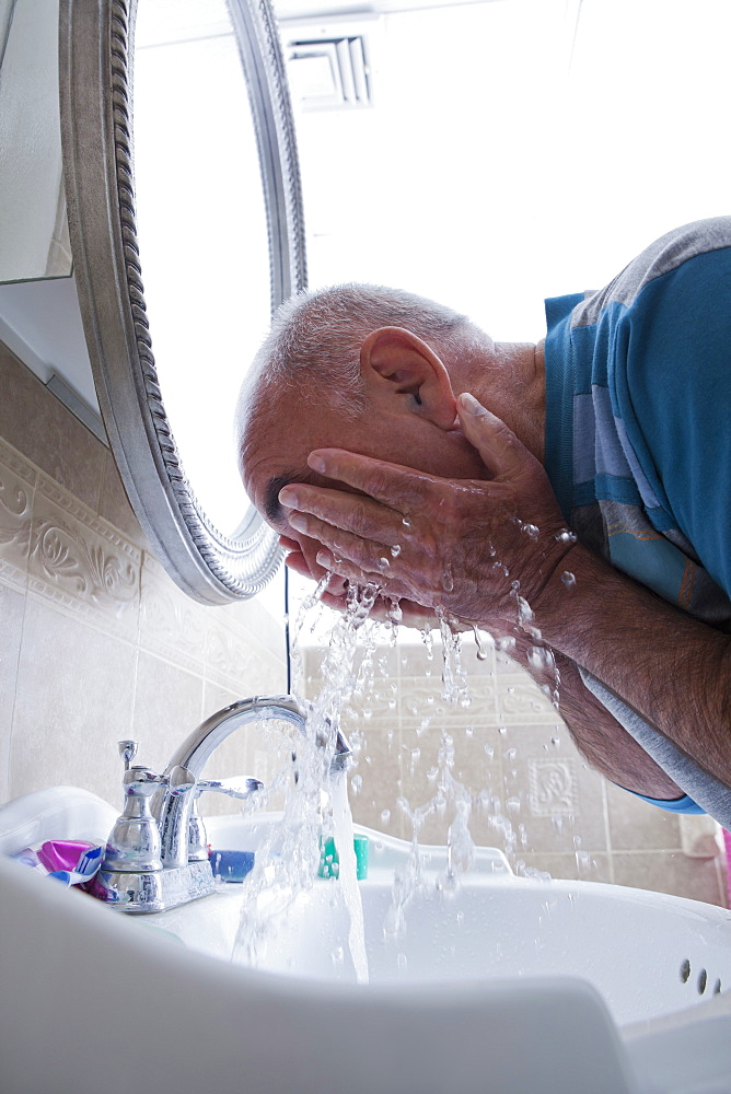 Hispanic man splashing water on face in bathroom