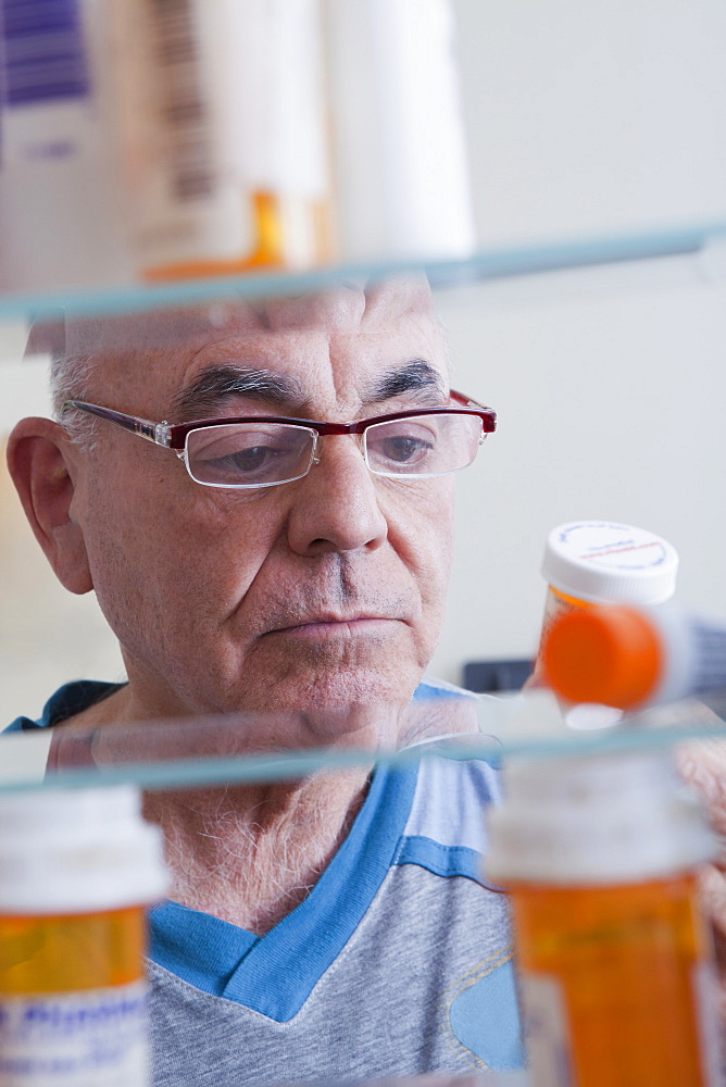 Hispanic man examining pill bottle from medicine cabinet