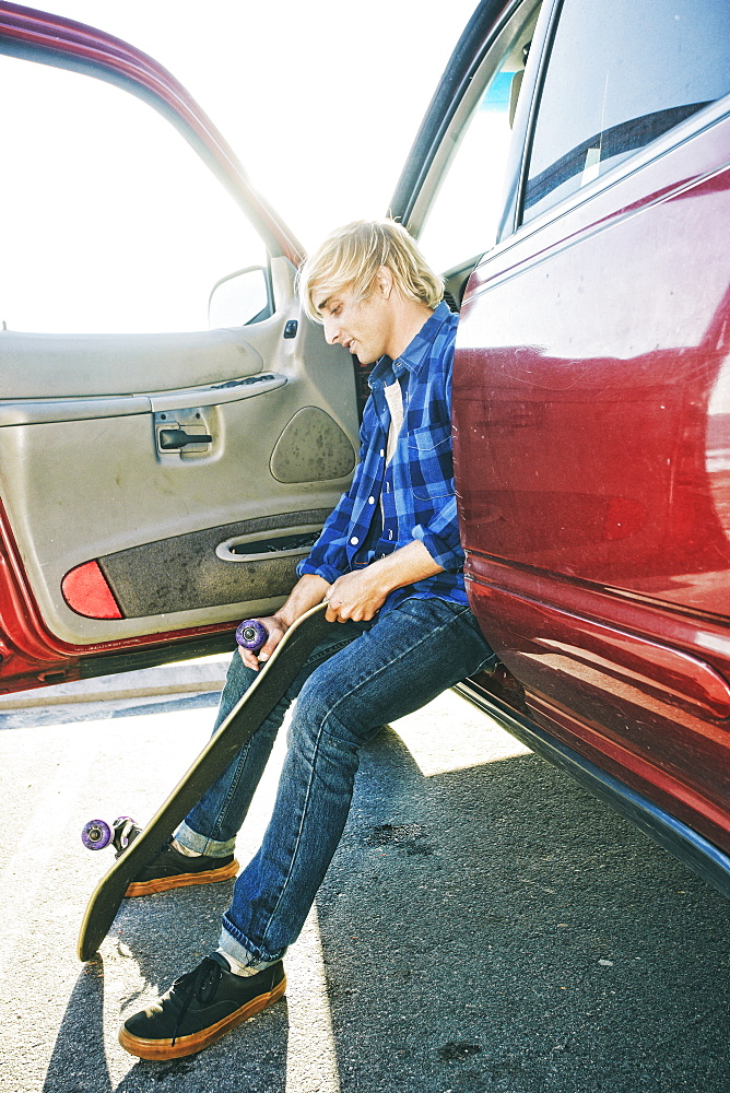 Caucasian man sitting in car holding skateboard wheel