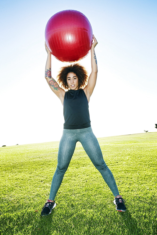 Hispanic woman exercising with fitness ball in sunny field