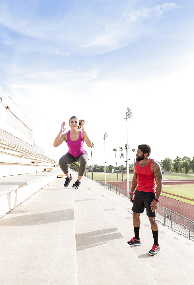 Trainer watching woman jumping on bleachers