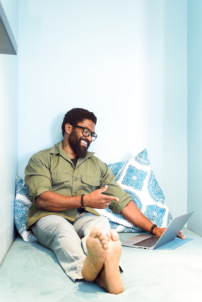 Smiling black man sitting on bed pointing at laptop