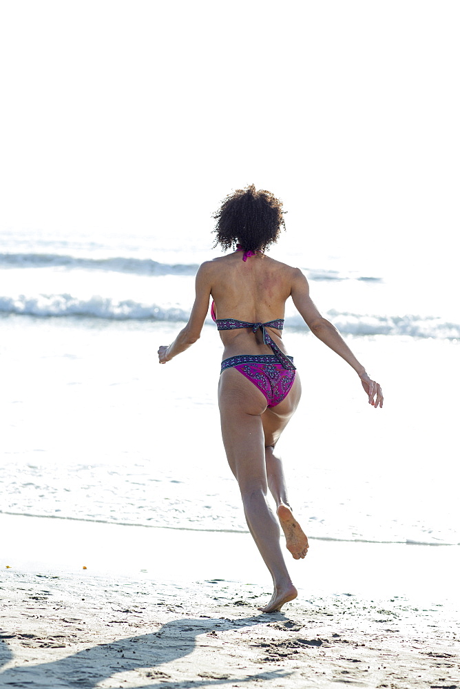 Mixed Race woman wearing bikini running to ocean