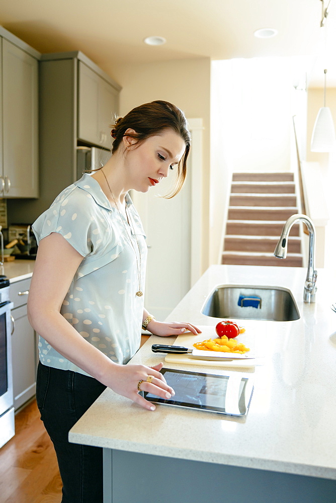 Woman using digital tablet and chopping food in domestic kitchen