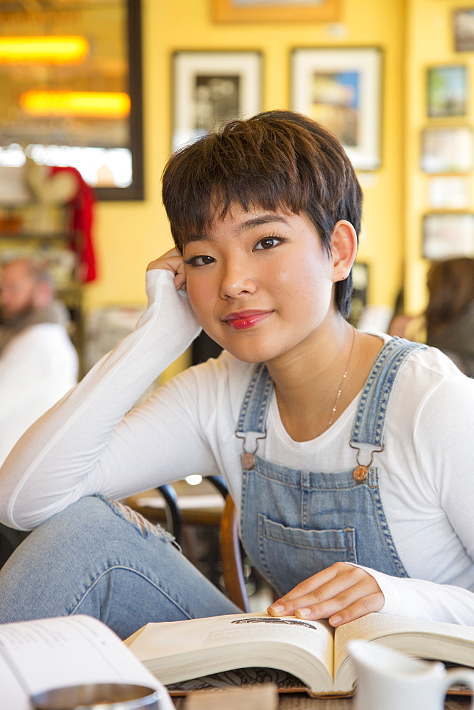 Asian teenage girl reading book in coffee shop