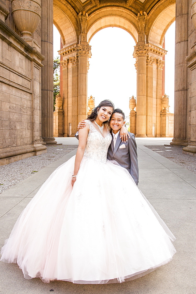 Hispanic girl wearing gown hugging boy