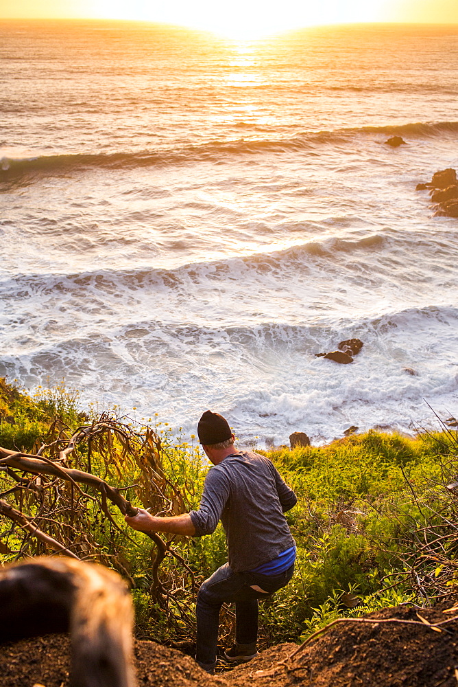 Caucasian man descending hill near ocean at sunset