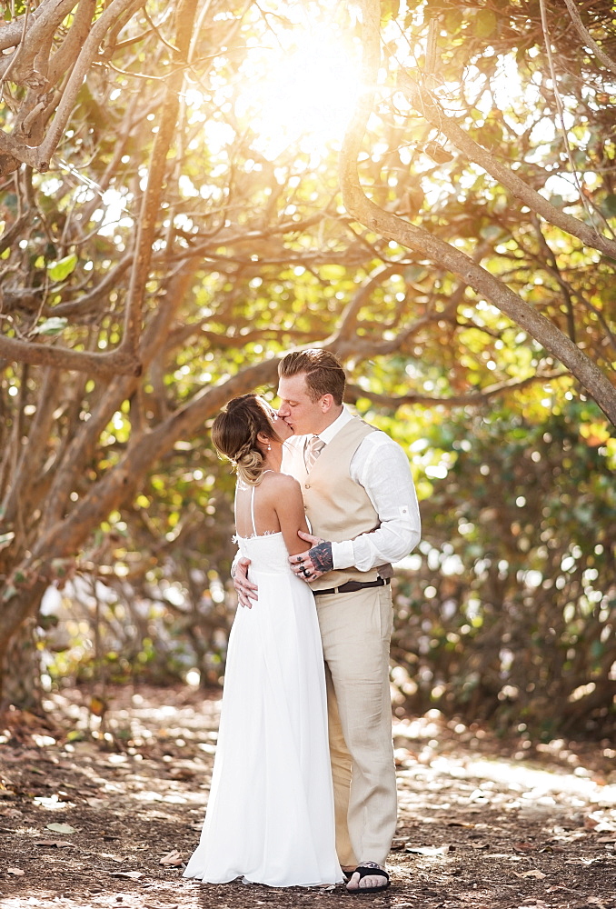 Caucasian bride and groom kissing under trees