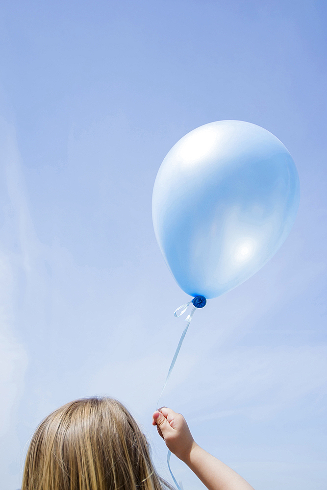 Caucasian girl holding blue balloon in blue sky