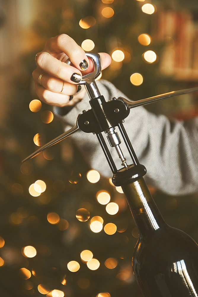 Hand of Caucasian woman opening wine bottle with corkscrew