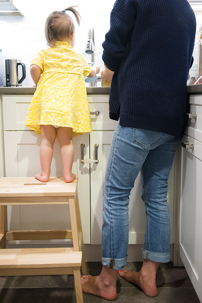 Caucasian baby girl helping mother washing dishes