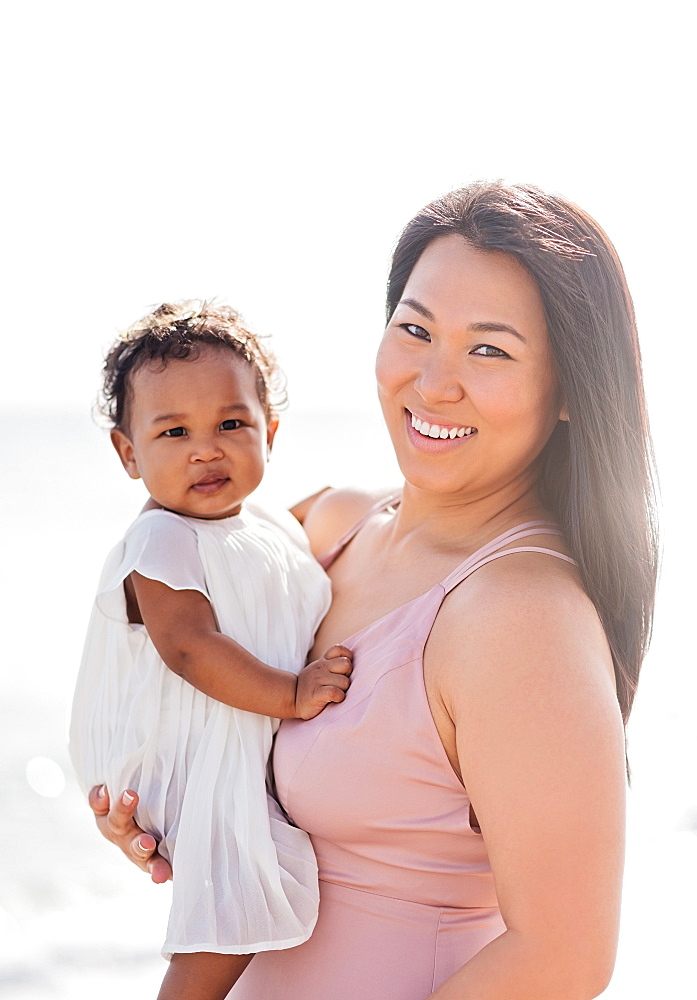 Portrait of mother holding baby daughter near ocean