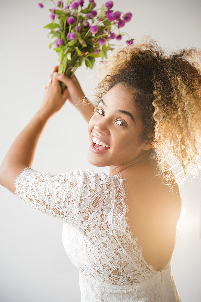 Mixed Race woman wearing wedding dress tossing bouquet