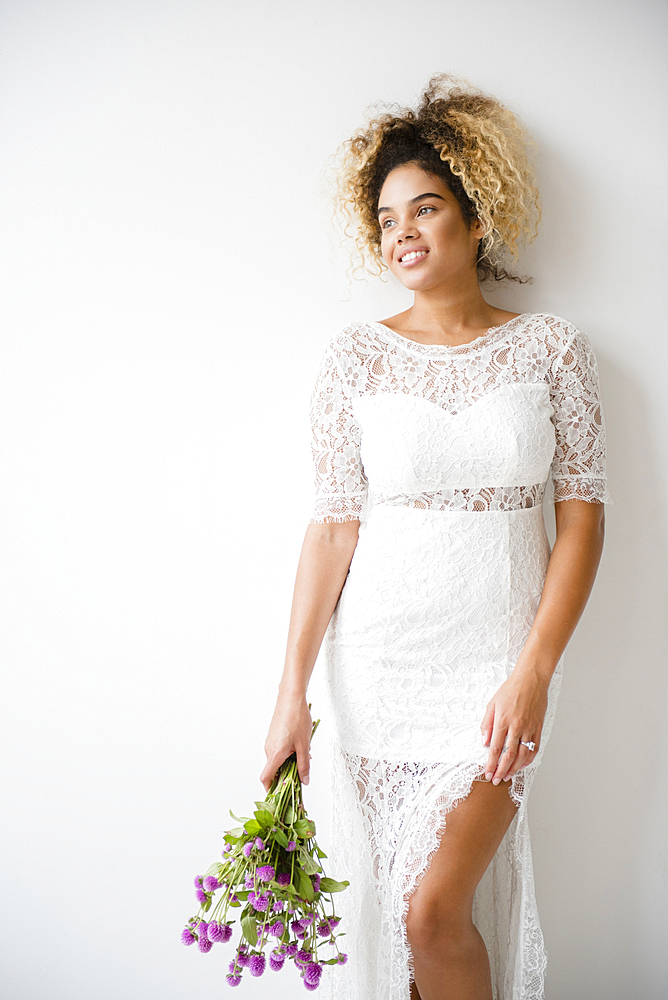 Mixed Race woman wearing wedding dress leaning on wall