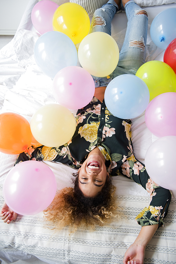 Mixed Race woman laying on bed covered with balloons