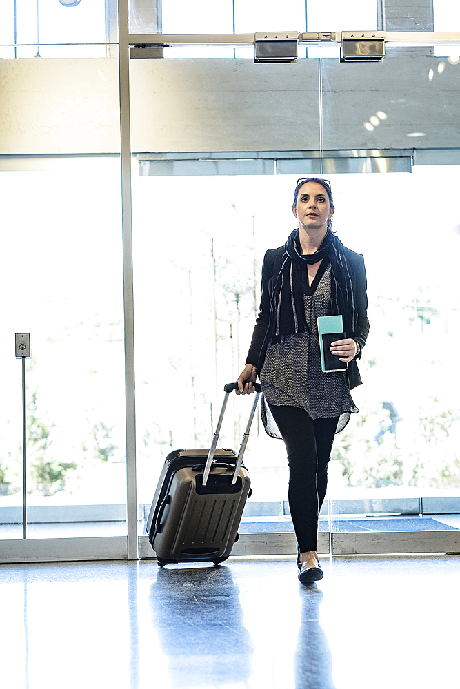 Hispanic woman holding passport pulling suitcase in airport