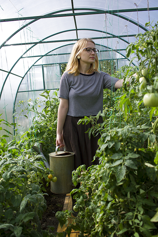 Caucasian woman with watering can examining plants in greenhouse