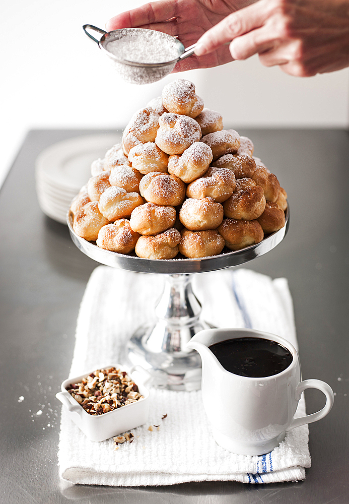 Hands shaking powdered sugar onto tray of cream puffs