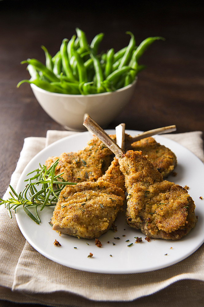 Breaded lamb chops on plate with bowl of green beans