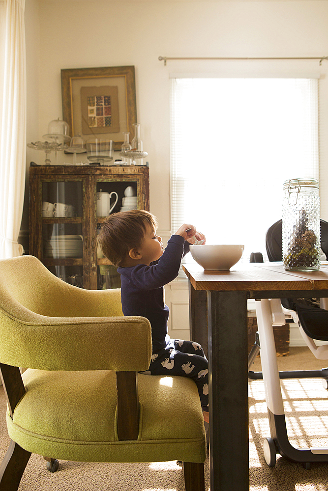 Mixed Race boy sitting at table eating from high bowl