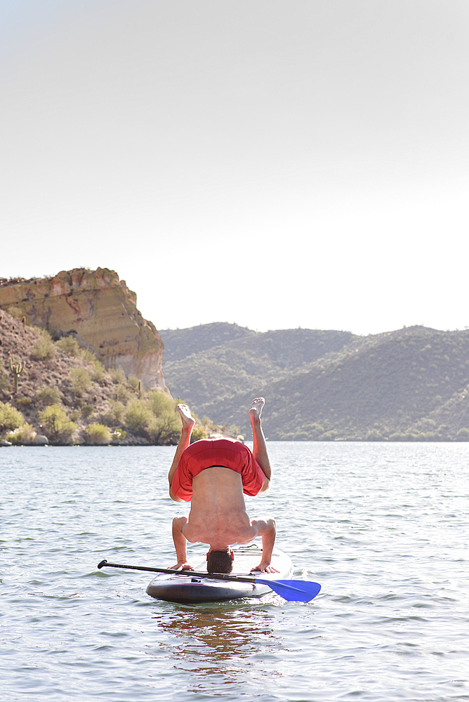 Hispanic man doing headstand on paddleboard in river