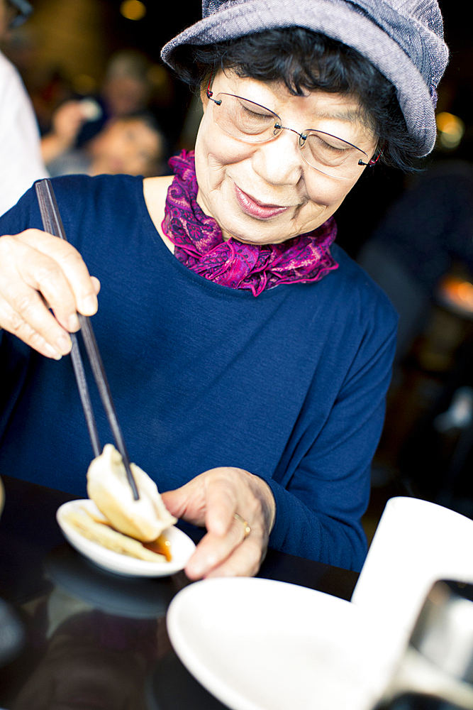 Older Japanese woman eating food with chopsticks